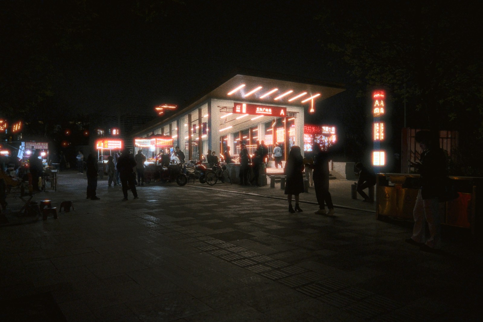 People gather at a brightly lit cafe at night.