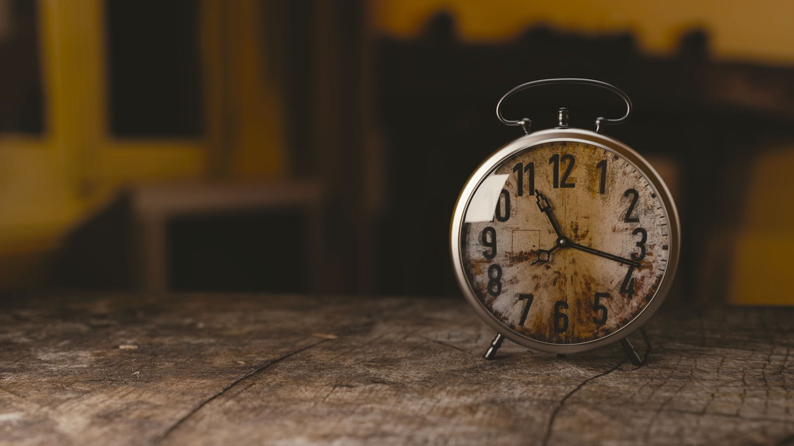 A classic vintage alarm clock sits on a rustic wooden table indoors.